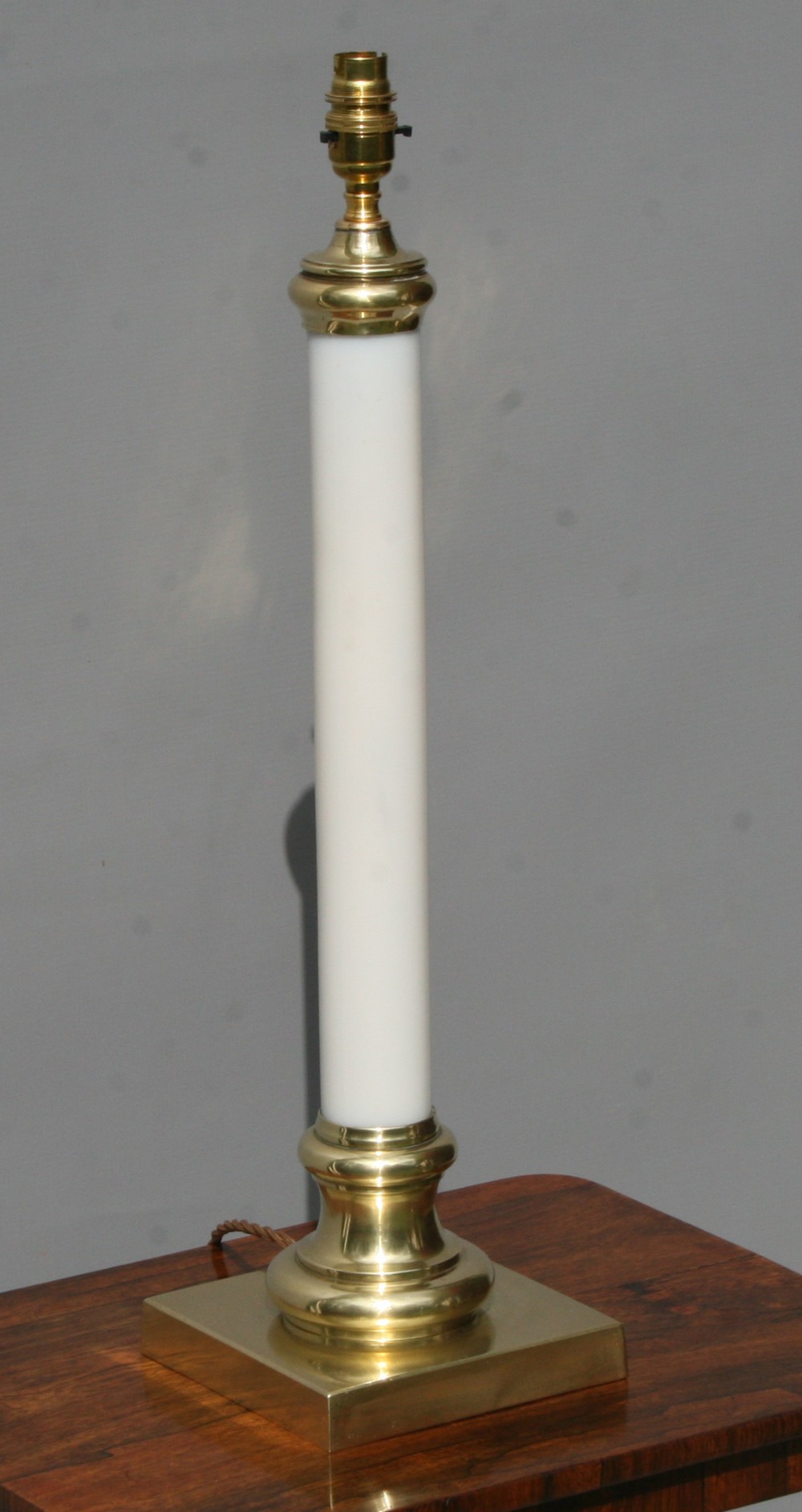 A tall Victorian table lamp featuring a straight white opaline glass column mounted on a square brass base with turned brass fittings.