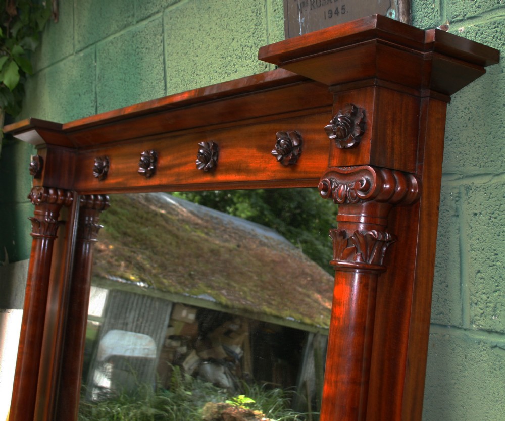 An early Victorian flame mahogany overmantel mirror featuring side columns with carved Corinthian capitals and a frieze decorated with carved rosettes. View VI