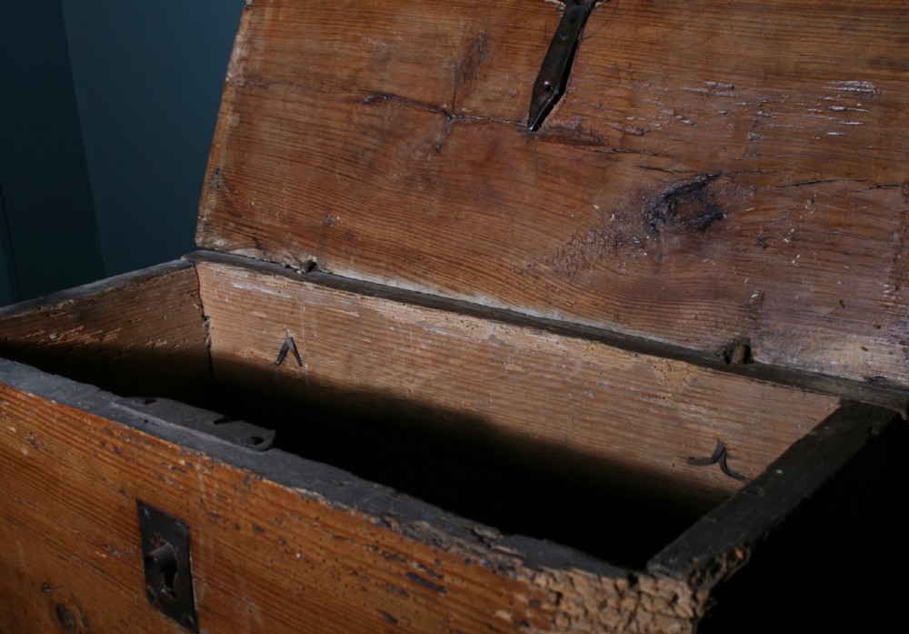 A rustic pine chest featuring exposed dovetail joints, a central iron keyhole plate, a scalloped lower apron, and carved wooden feet. View V