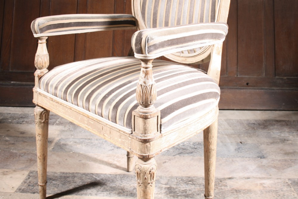 An antique French Louis XVI style upholstered armchair featuring a painted timber frame, oval backrest, padded armrests, turned fluted legs, and grey striped fabric. View IV