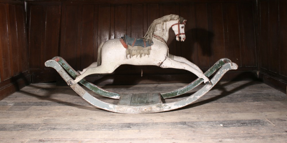 A 19th-century hand-carved wooden rocking horse in off-white painted finish mounted on green curved wooden bow rockers.