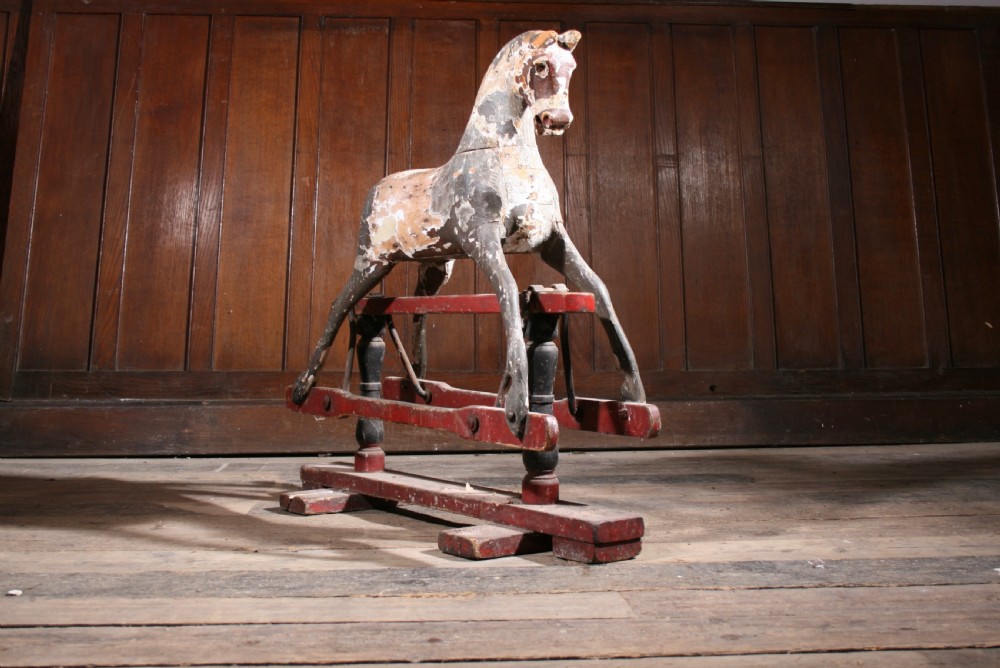 A carved wooden antique rocking horse with distressed grey original paint mounted on a red glider stand. View V