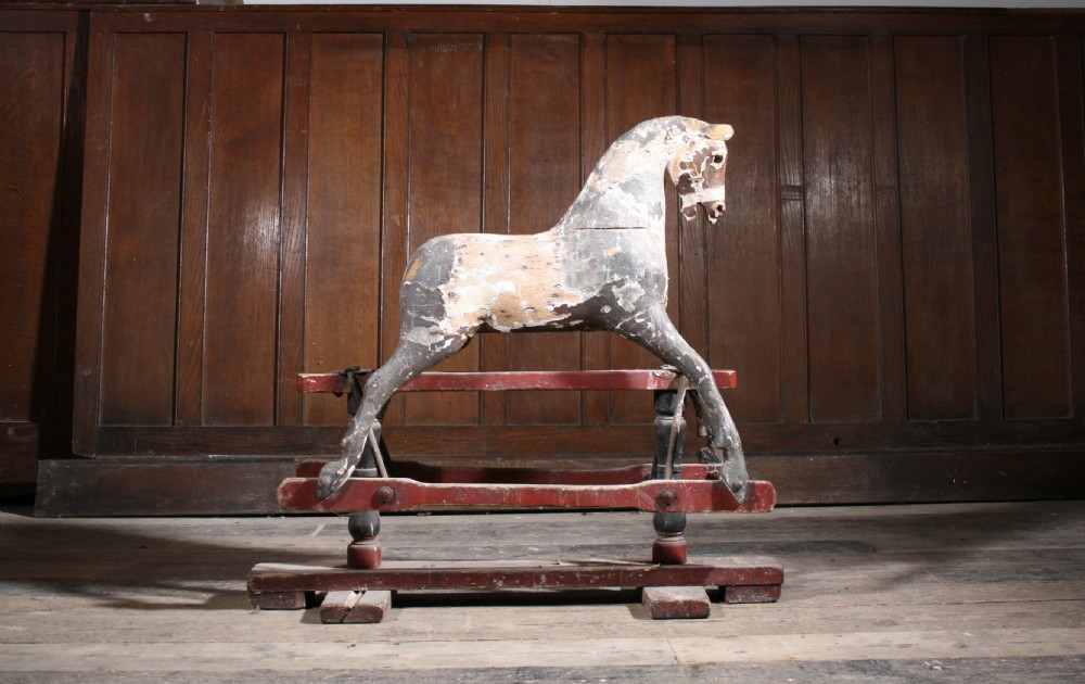 A carved wooden antique rocking horse with distressed grey original paint mounted on a red glider stand. View VI