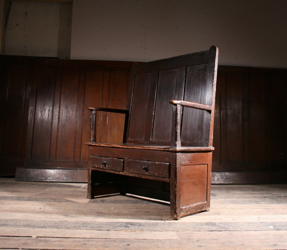 A dark brown Georgian pine settle with a high panelled back, straight wooden armrests, and two drawers set into the base. View III