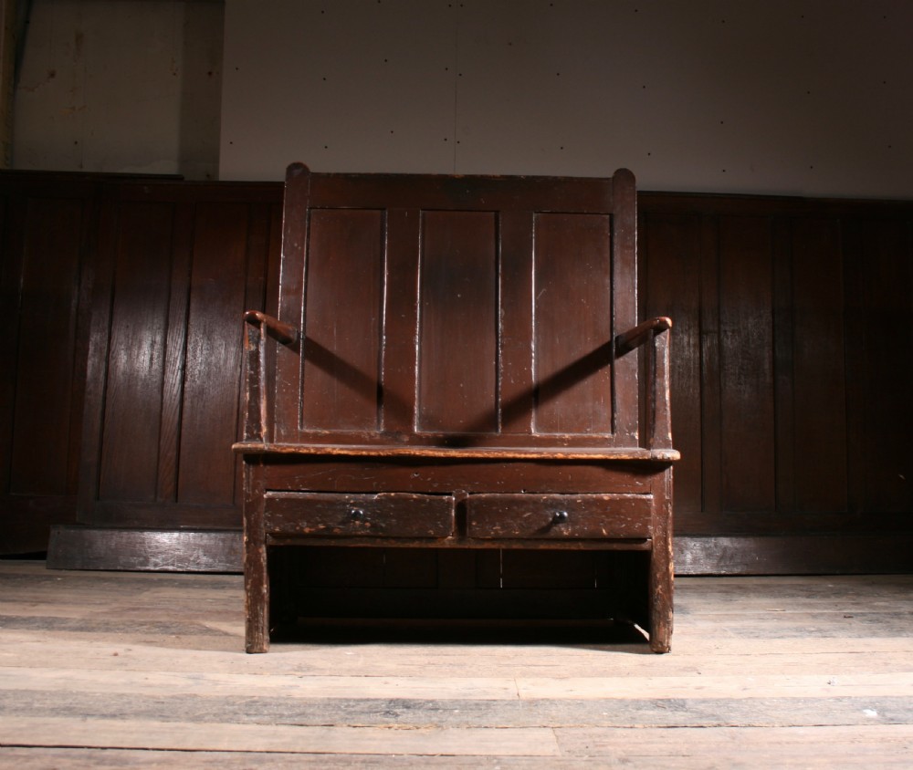 A dark brown Georgian pine settle with a high panelled back, straight wooden armrests, and two drawers set into the base. View V