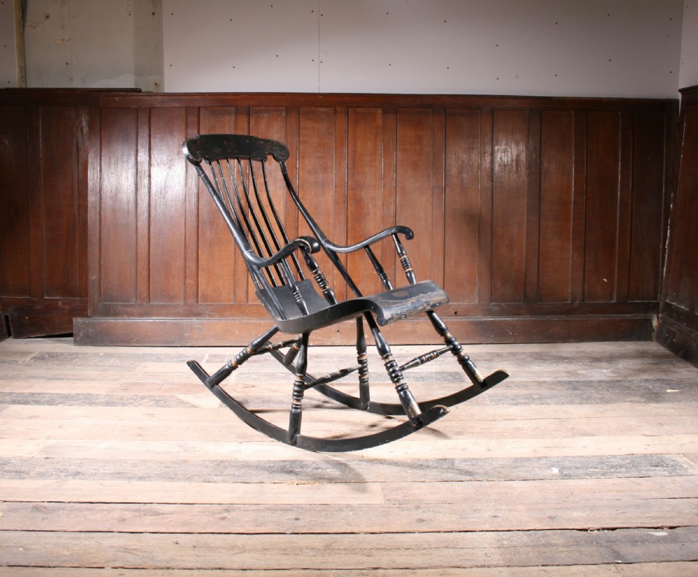 A Swedish painted wood rocking chair with a spindle back, curved armrests, turned legs, and a black distressed finish.