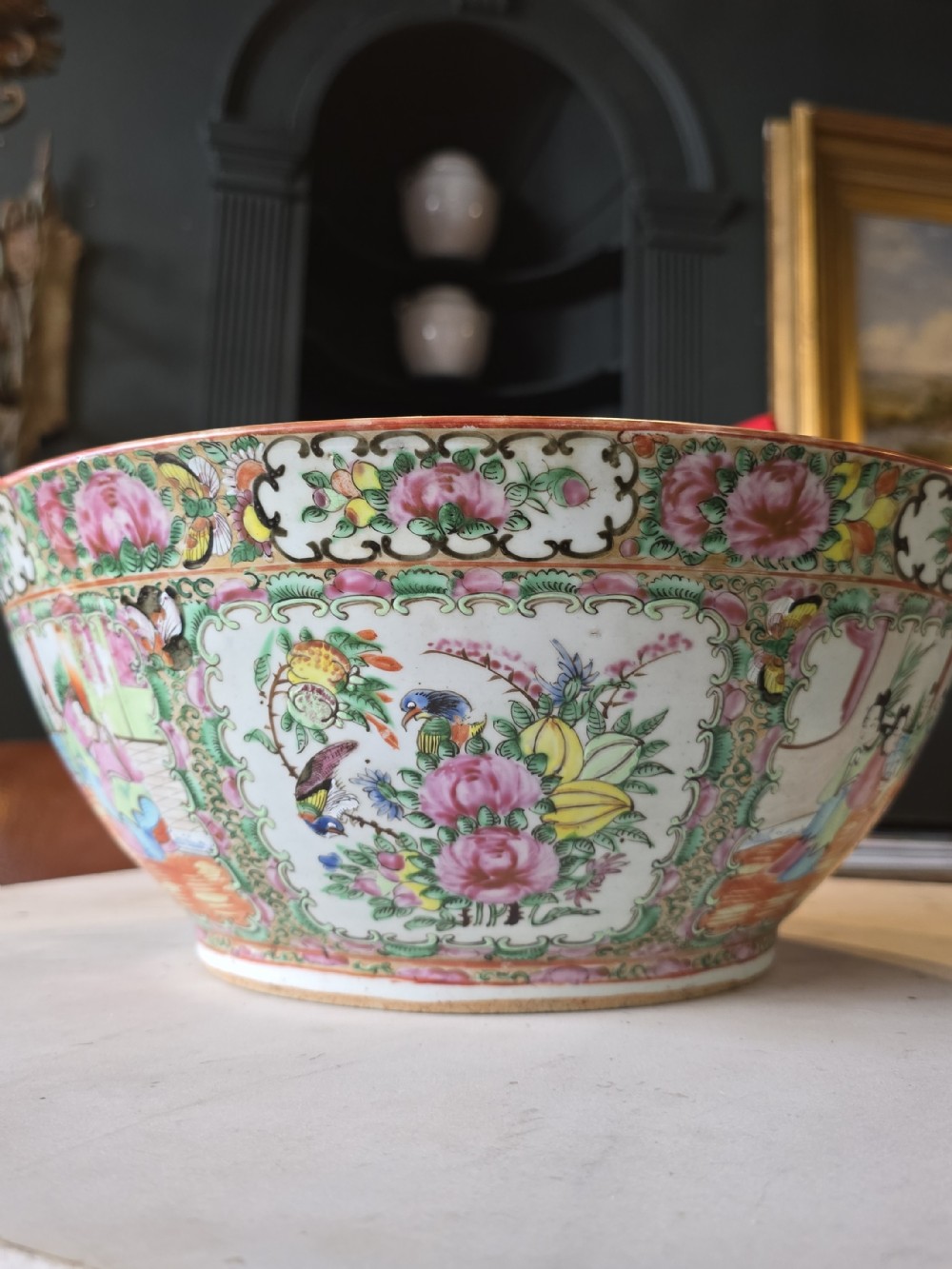 A large deep porcelain punch bowl decorated with hand-painted Chinese Famille Rose enamel motifs, featuring figures, flora, birds, and butterflies within reserves.