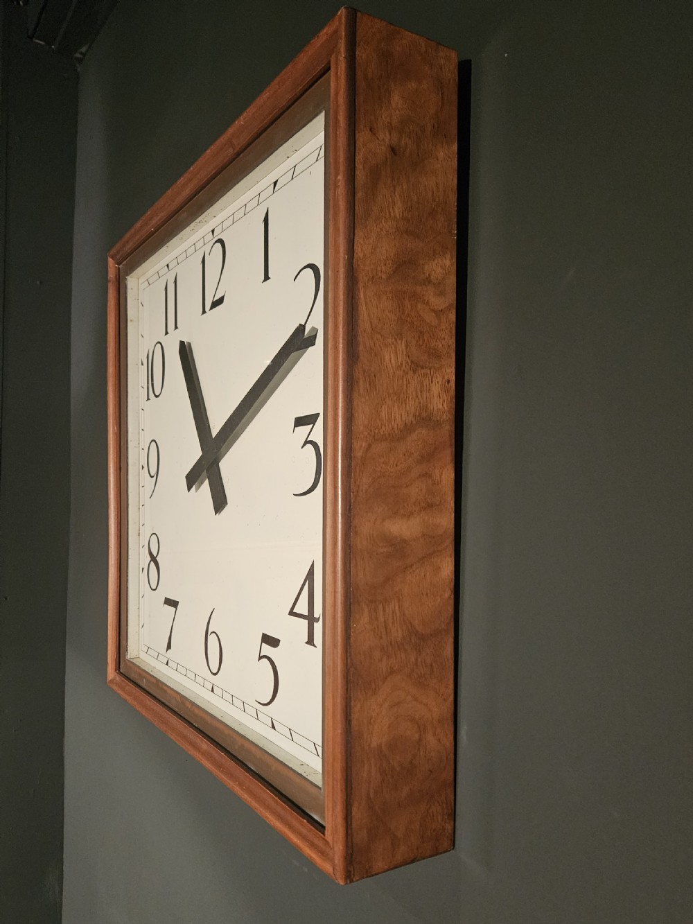 A square wall clock featuring a walnut wood frame, a copper inner border, and a white dial with black Arabic numerals. View II