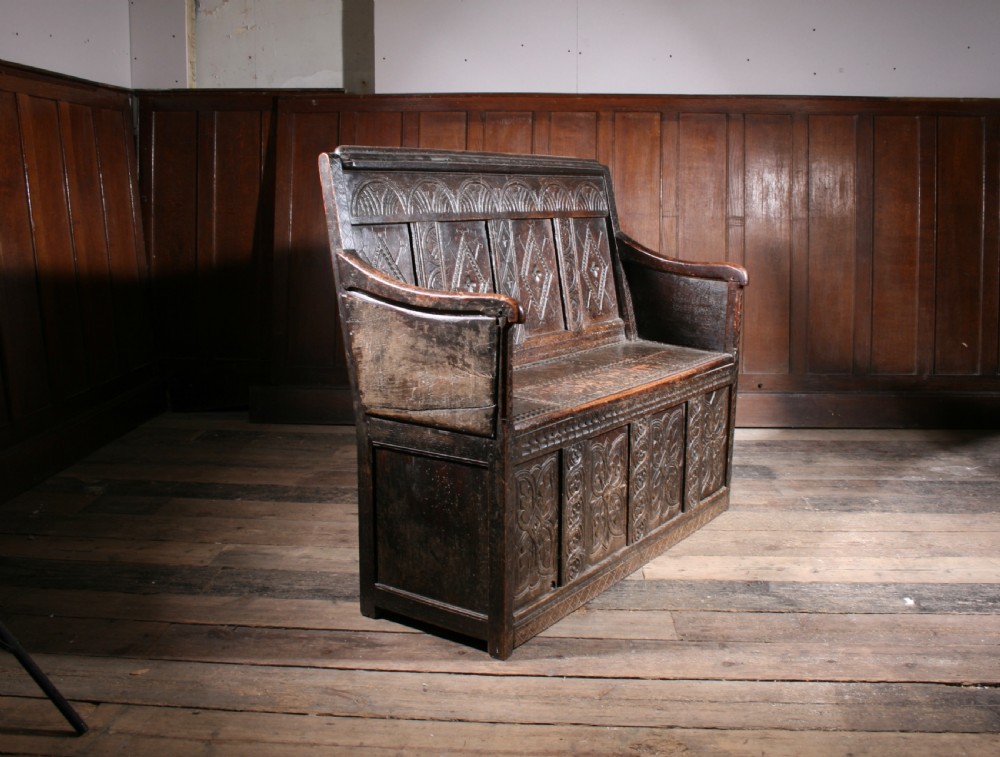 A dark brown 17th-century carved oak settle with high panelled back featuring diamond lozenge carvings and a wooden bench seat. View II