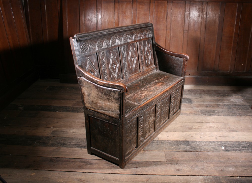 A dark brown 17th-century carved oak settle with high panelled back featuring diamond lozenge carvings and a wooden bench seat. View III