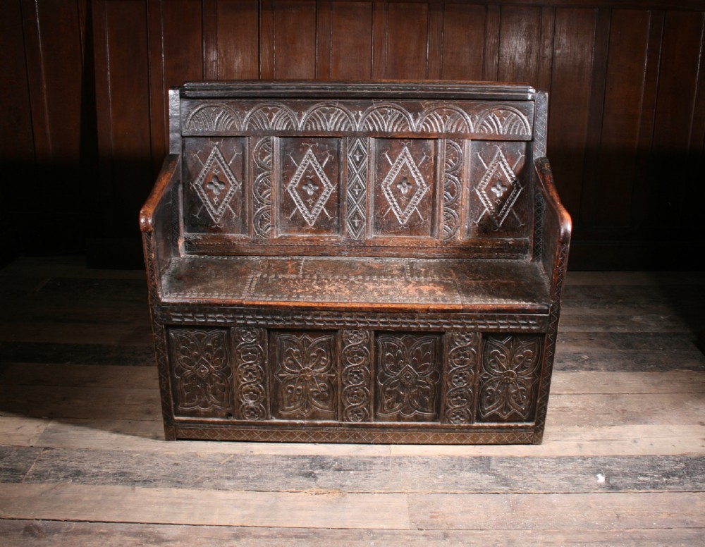 A dark brown 17th-century carved oak settle with high panelled back featuring diamond lozenge carvings and a wooden bench seat. View V