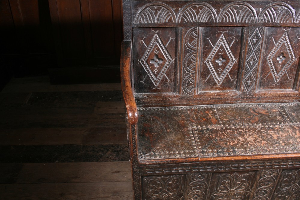A dark brown 17th-century carved oak settle with high panelled back featuring diamond lozenge carvings and a wooden bench seat. View VI