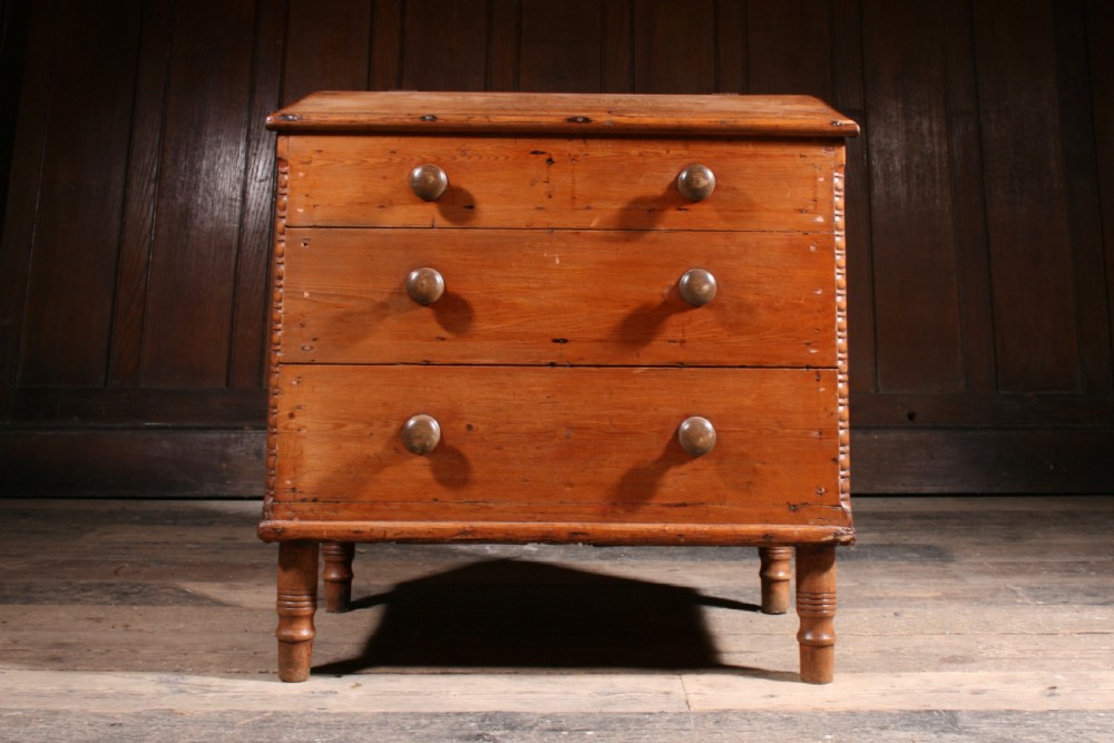 A Georgian pine mule chest featuring a hinged top lid, three lower drawer fronts with turned wooden knobs, and turned legs.