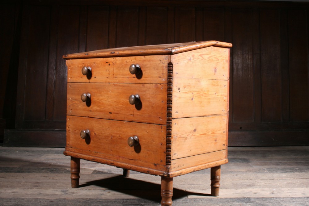 A Georgian pine mule chest featuring a hinged top lid, three lower drawer fronts with turned wooden knobs, and turned legs. View VII