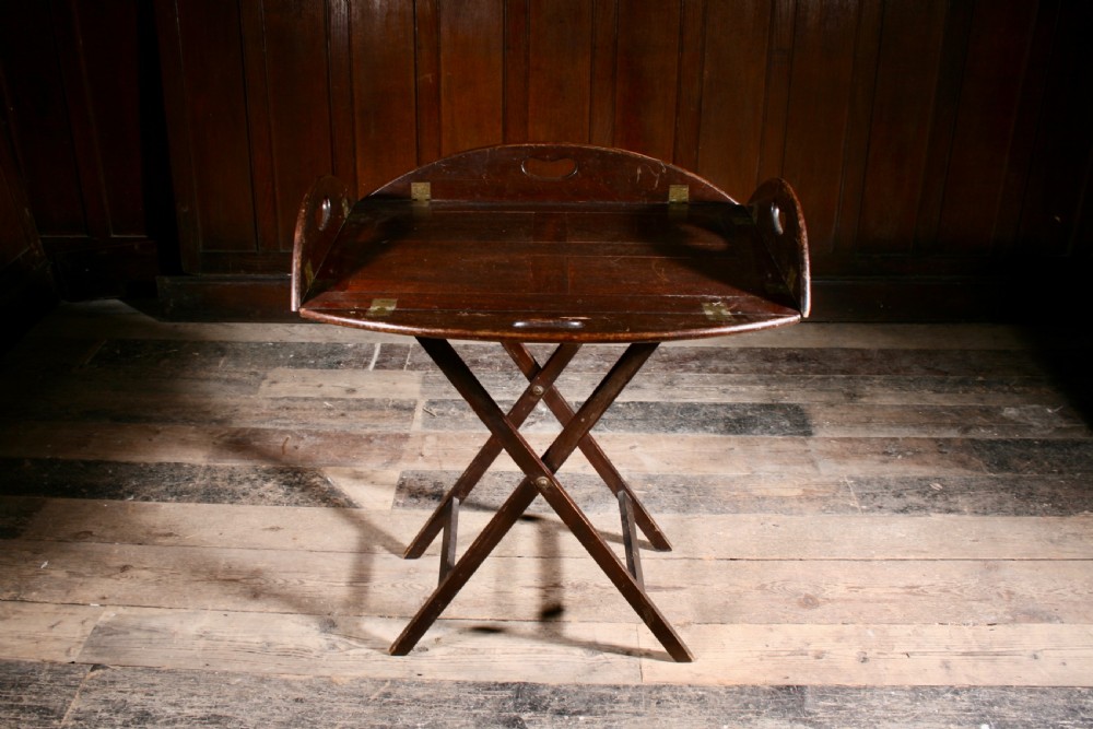A dark mahogany Georgian butler tray with folding sides and brass hinges resting atop a matching wooden X-frame folding stand.