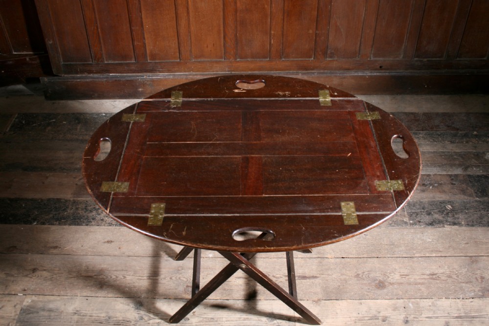 A dark mahogany Georgian butler tray with folding sides and brass hinges resting atop a matching wooden X-frame folding stand. View II