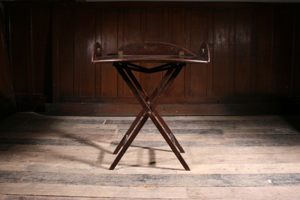 A dark mahogany Georgian butler tray with folding sides and brass hinges resting atop a matching wooden X-frame folding stand. View III