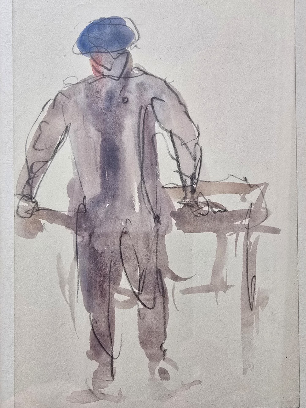 An original watercolour and ink figure study on paper depicting a man in a blue cap seen from behind leaning over a surface.