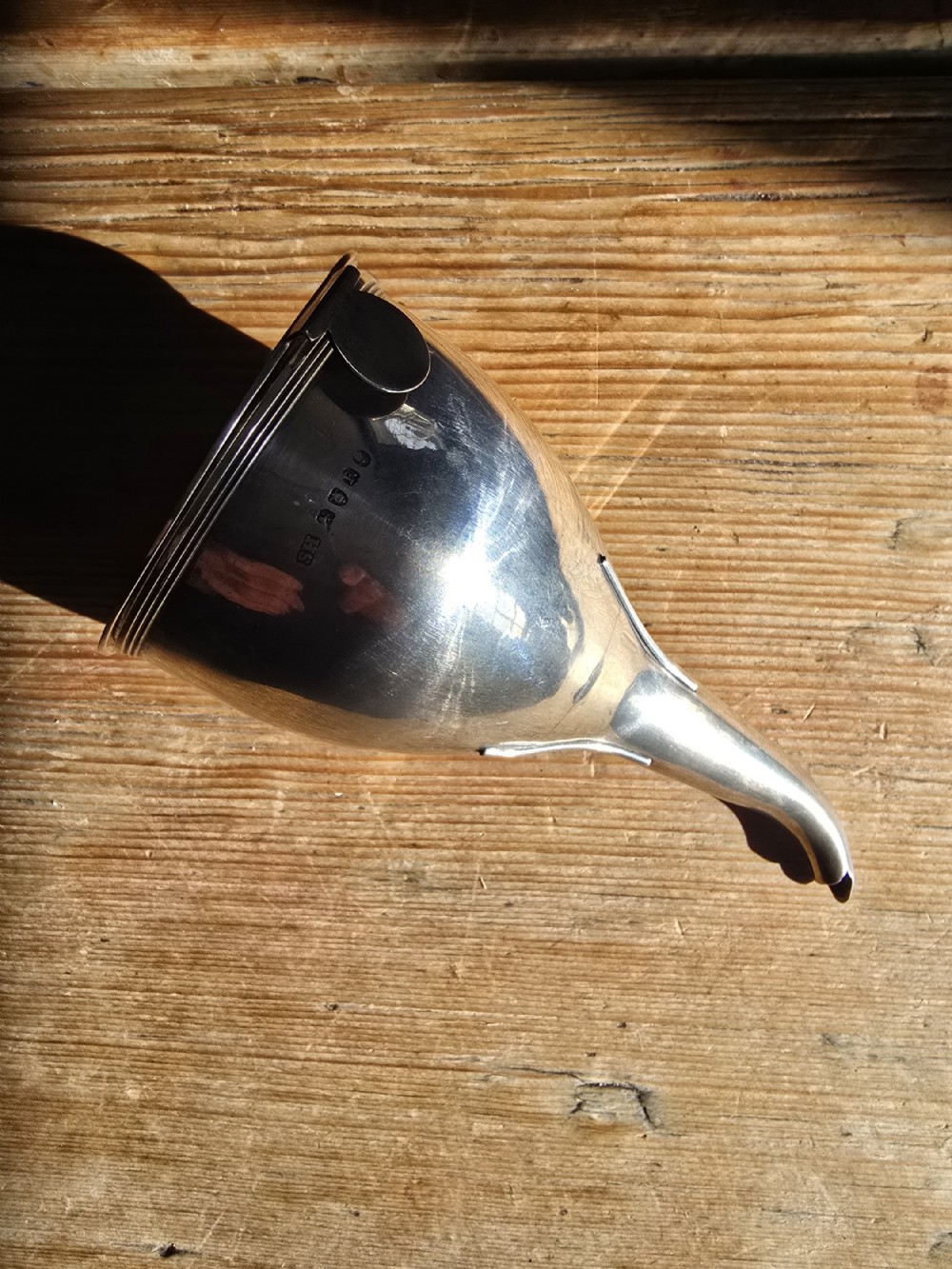 A polished Georgian sterling silver wine funnel featuring a reeded rim, side clip, curved spout, and stamped London hallmarks.