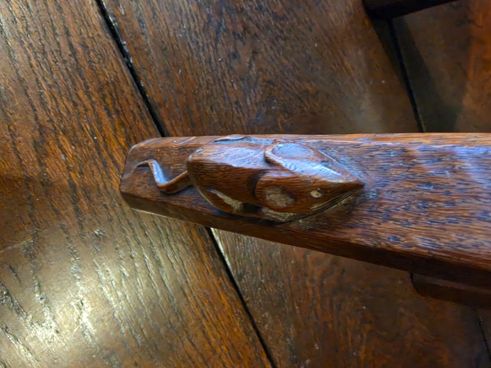 A dark English oak three-legged stool featuring an adzed kidney-shaped seat and a hand-carved mouse motif on one leg. View V