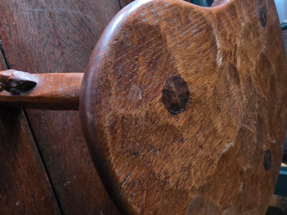 A dark English oak three-legged stool featuring an adzed kidney-shaped seat and a hand-carved mouse motif on one leg. View VI