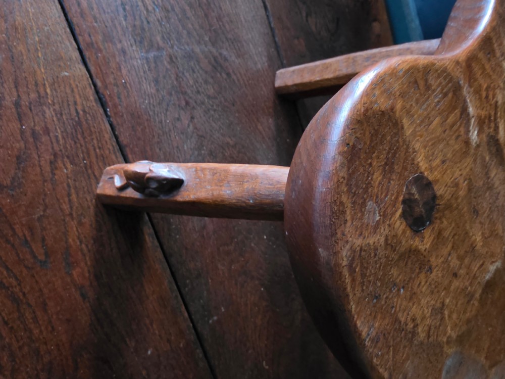 A dark English oak three-legged stool featuring an adzed kidney-shaped seat and a hand-carved mouse motif on one leg. View VII