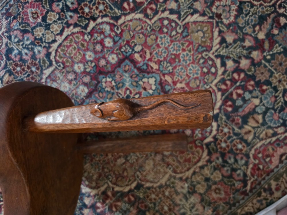 A dark English oak three-legged stool featuring an adzed kidney-shaped seat and a hand-carved mouse motif on one leg. View X
