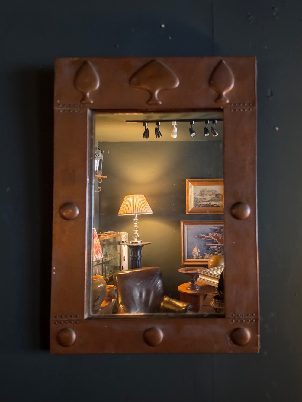A rectangular Arts and Crafts wall mirror featuring a hammered copper frame decorated with embossed stylised tree motifs and raised roundels.