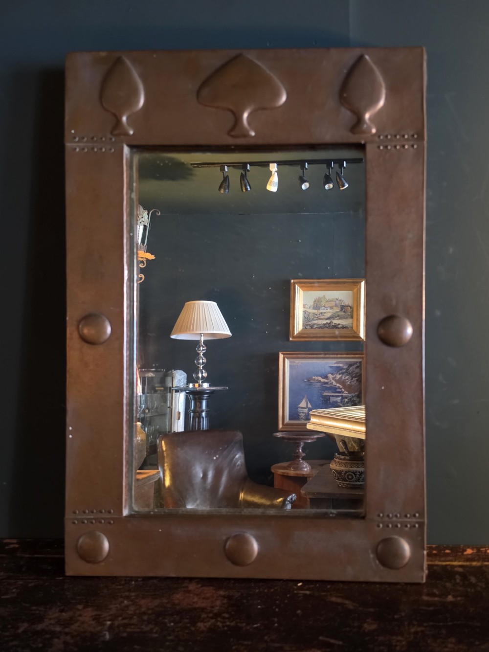 A rectangular Arts and Crafts wall mirror featuring a hammered copper frame decorated with embossed stylised tree motifs and raised roundels. View II