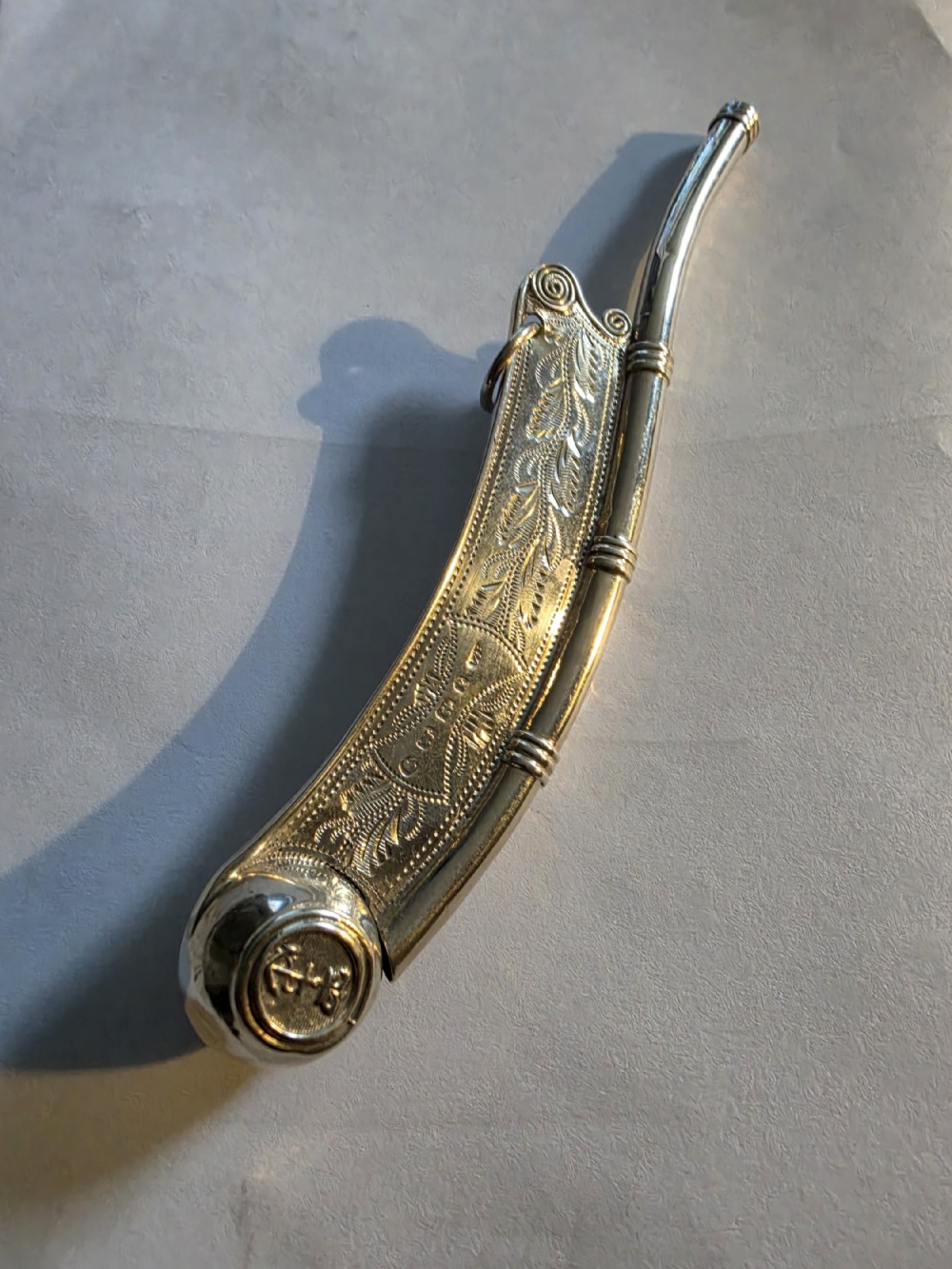 A Victorian sterling silver boatswain whistle featuring engraved foliate decoration along the curved keel, a stamped anchor crest on the buoy, and a suspension ring.