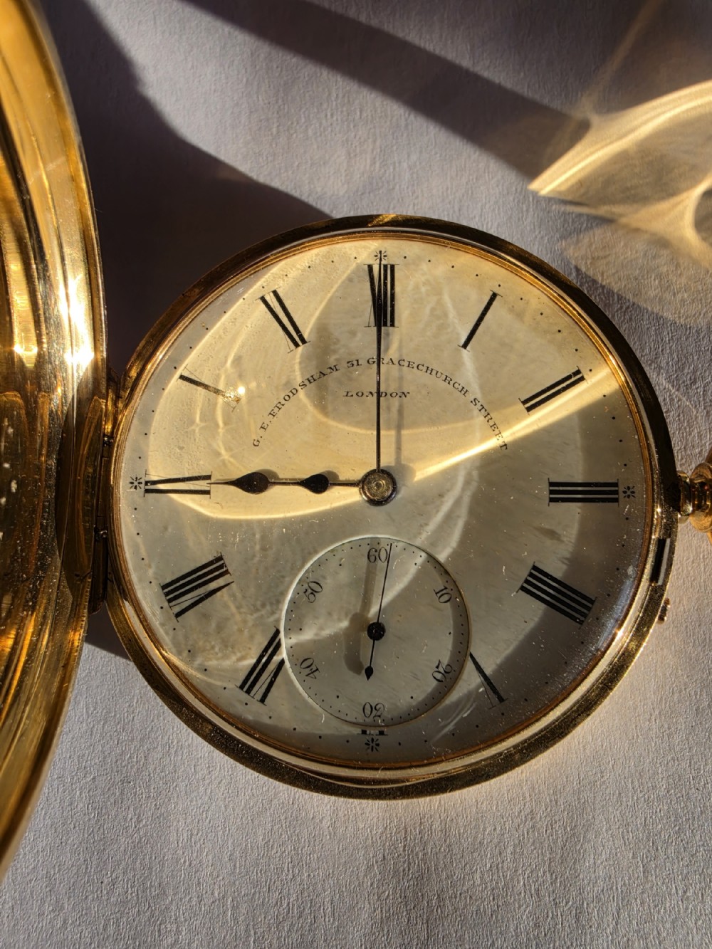 An open 18 carat yellow gold half hunter pocket watch displaying a white enamel dial with black Roman numerals and a subsidiary seconds subdial.