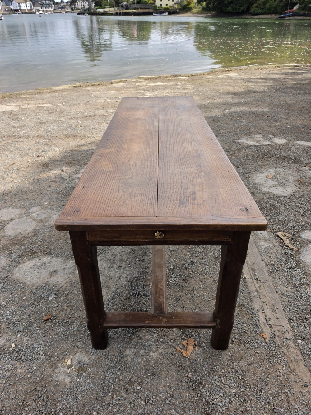An eighteenth-century chestnut dining table featuring a long twin-plank surface, an end drawer with a brass keyhole escutcheon, and an H-stretcher base.
