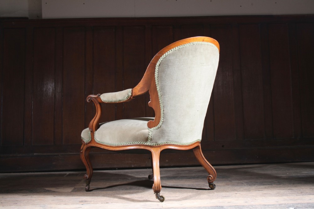 An antique walnut library armchair upholstered in button-tufted sage green velvet with carved cabriole legs on brass castors. View II