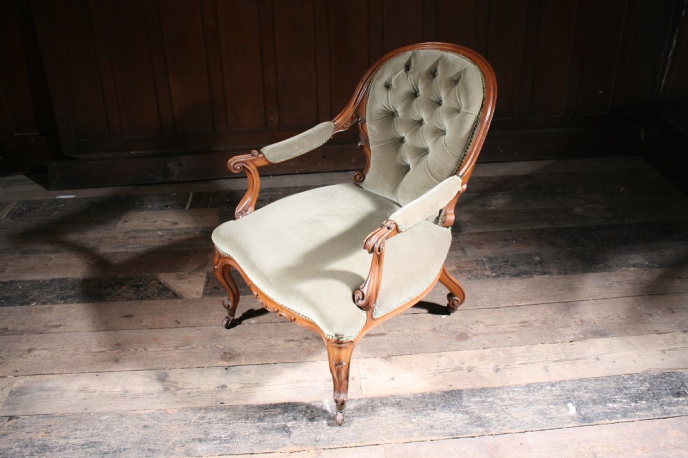 An antique walnut library armchair upholstered in button-tufted sage green velvet with carved cabriole legs on brass castors. View III