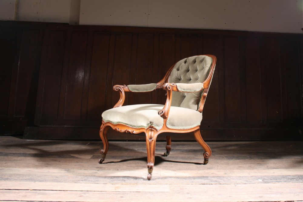 An antique walnut library armchair upholstered in button-tufted sage green velvet with carved cabriole legs on brass castors. View IV