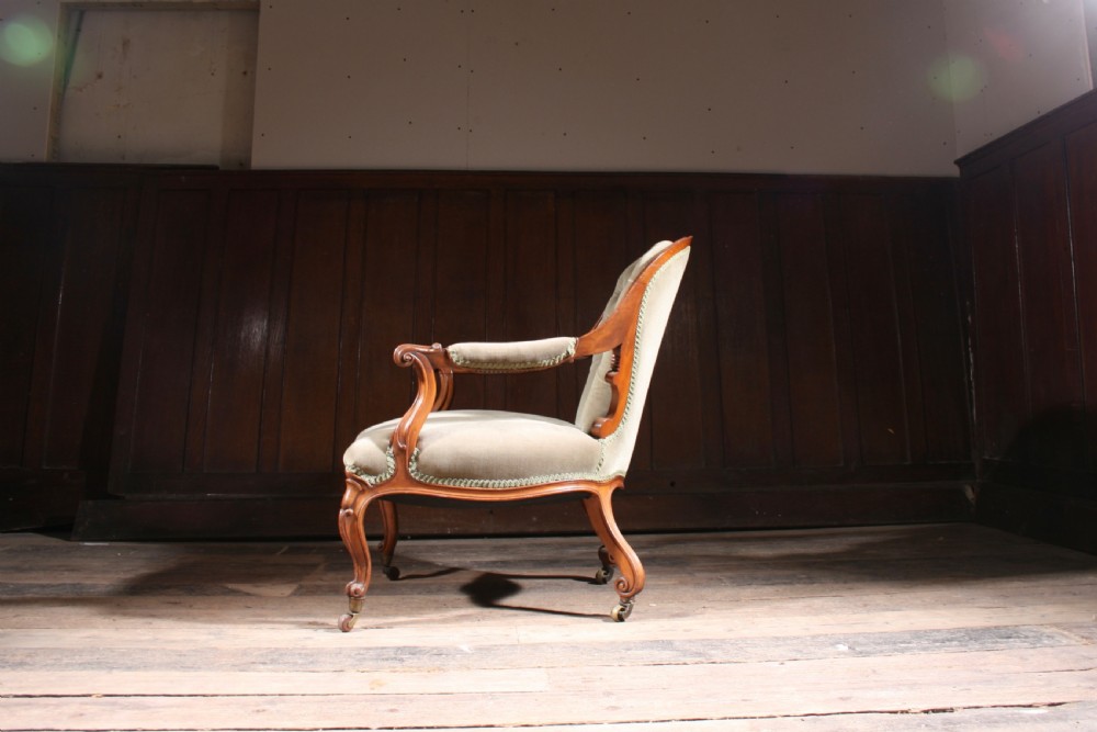 An antique walnut library armchair upholstered in button-tufted sage green velvet with carved cabriole legs on brass castors. View V