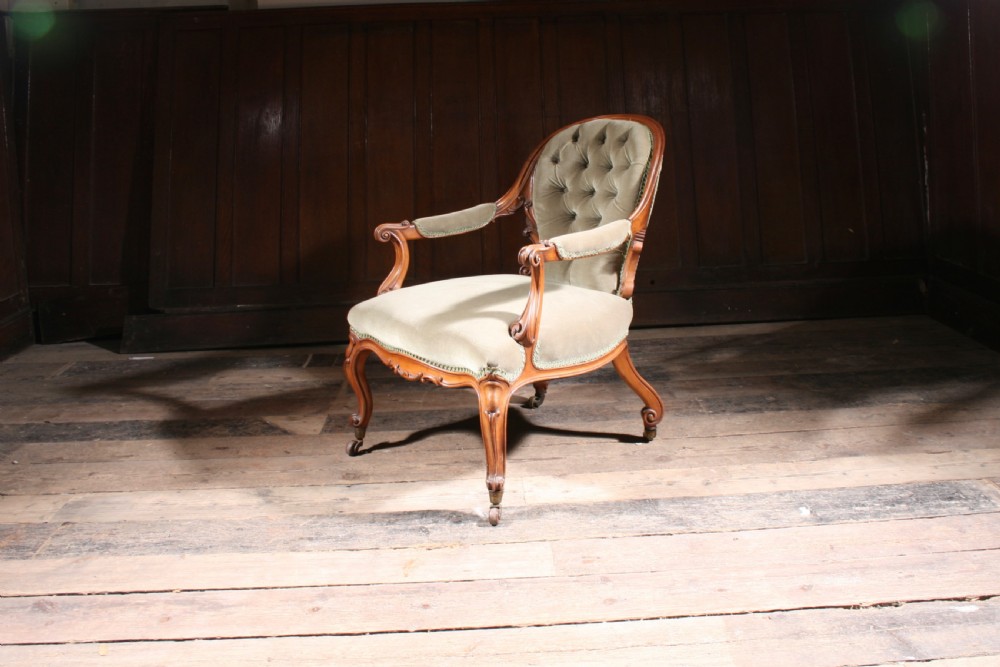 An antique walnut library armchair upholstered in button-tufted sage green velvet with carved cabriole legs on brass castors. View VI