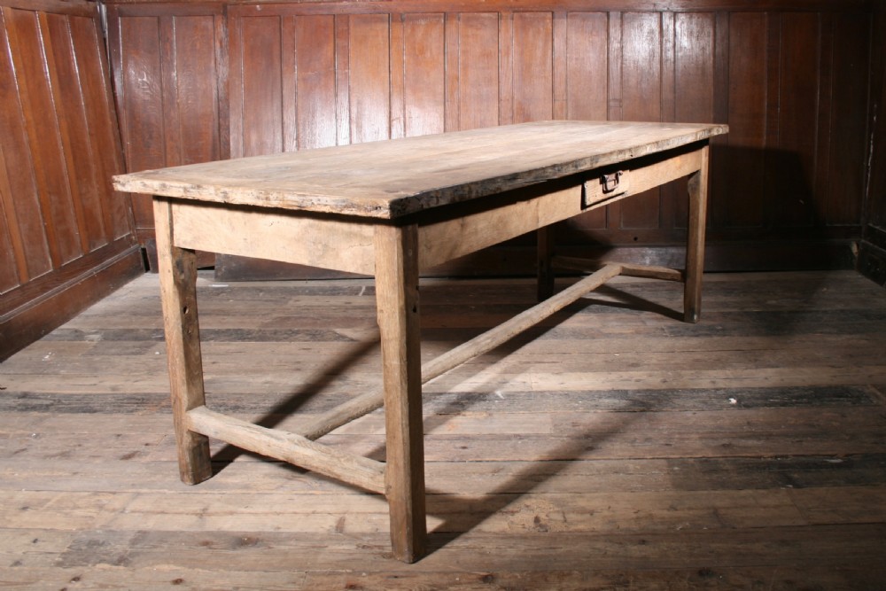 A long antique oak farmhouse dining table featuring a four-plank top, rectangular frame, square legs, and lower H-stretcher base. View IV