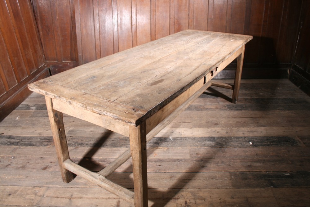 A long antique oak farmhouse dining table featuring a four-plank top, rectangular frame, square legs, and lower H-stretcher base. View V