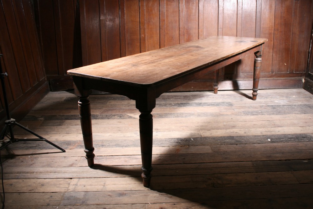 A long antique poplar farmhouse dining table featuring a twin-plank top supported by four turned wooden legs.