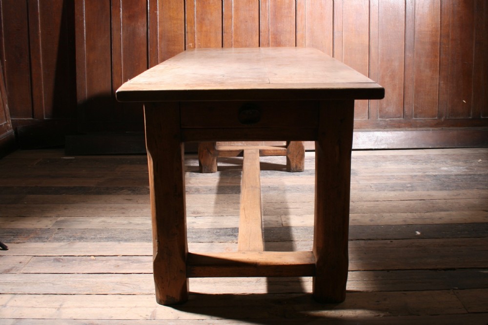 An antique walnut farmhouse dining table featuring a twin plank timber top, a single end drawer with a metal ring pull handle, and heavy legs connected by a central stretcher. View VI