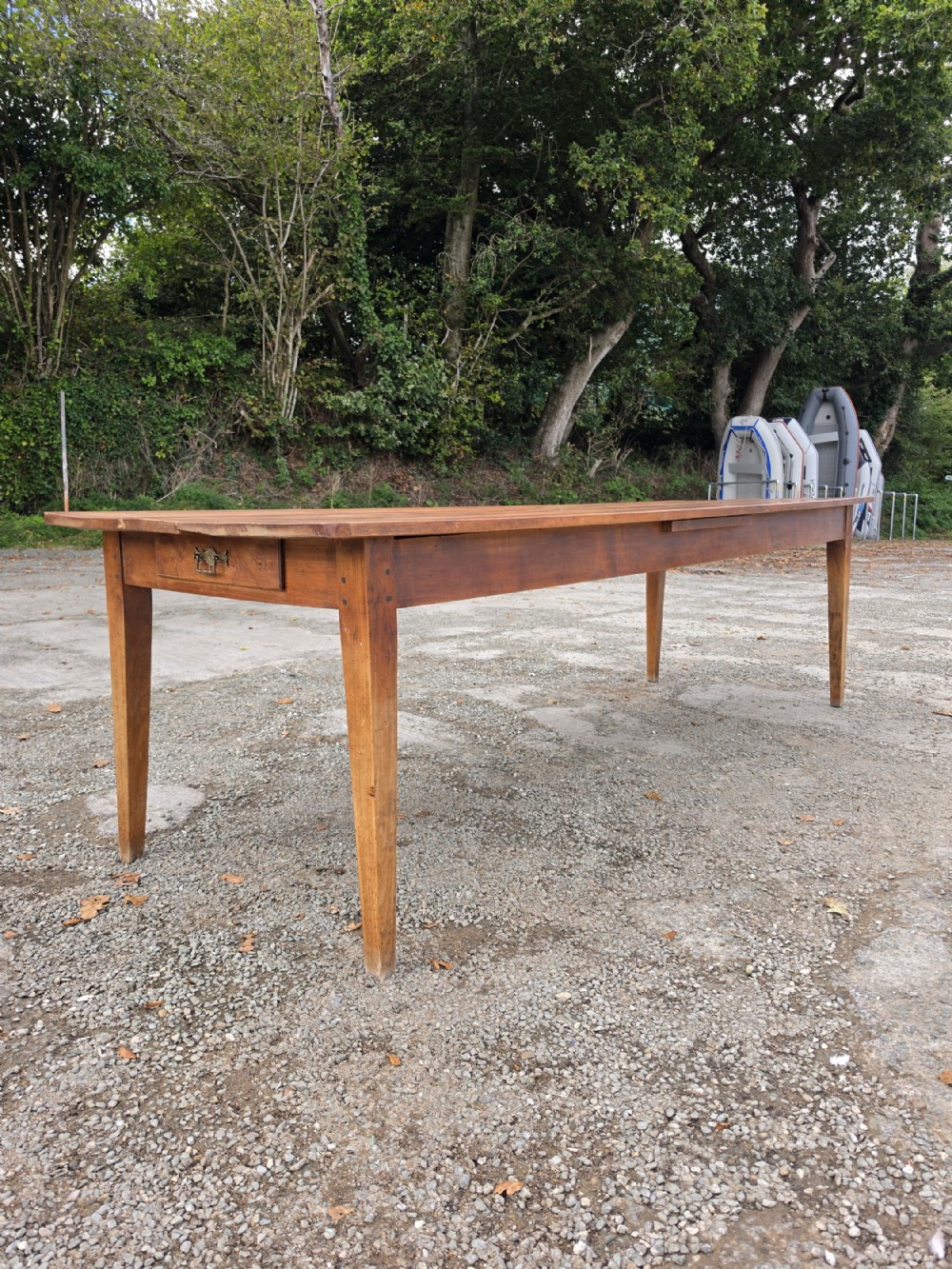 A long French provincial fruitwood farmhouse table featuring a plank top, single end drawer with a brass handle, and four tapered square legs.