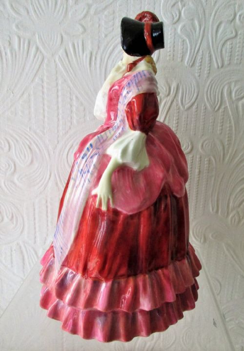 fig 1. A vintage Royal Doulton glazed bone china figurine depicting a lady in a red bonnet and layered red and pink crinoline dress with a patterned shawl.