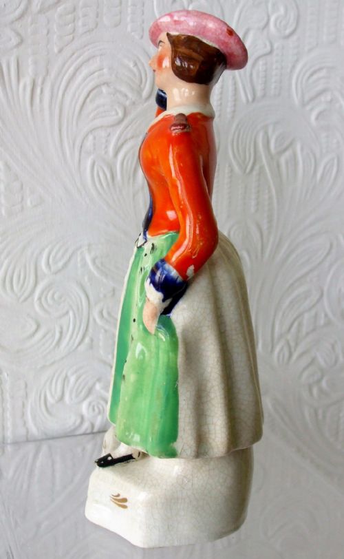fig 1. A Victorian Staffordshire earthenware figure of operatic performer Jenny Lind wearing an orange jacket, green skirt, and pink hat on a white base inscribed M. Lind.