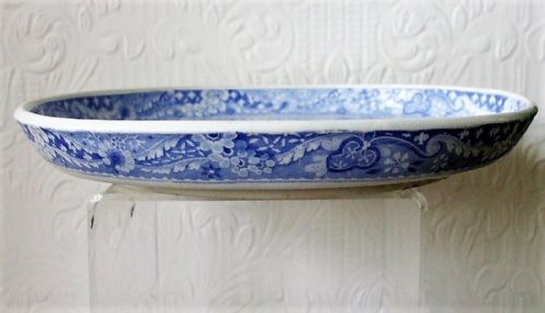 fig 1. A circular Georgian blue and white ceramic tazza decorated with a printed scene of a castle archway, stone bridge, trees, and figures within a floral border.