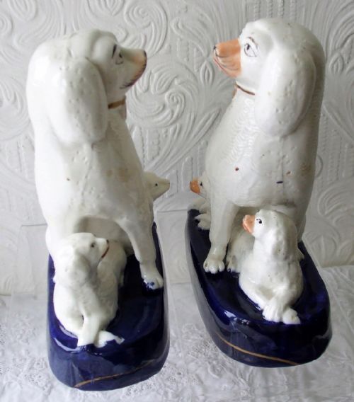 fig 1. A pair of white glazed earthenware Staffordshire poodle figurines seated on cobalt blue bases with puppies gathered at their feet.