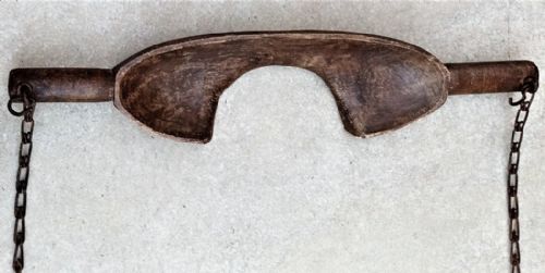fig 1. A carved dark beech wood shoulder yoke with a contoured neck arch and hanging iron chains with hooks on both ends.
