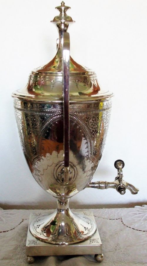 fig 1. An Edwardian silver-plated tea samovar featuring detailed engraved scrolling patterns, tall side handles, a spigot, and a pedestal base.