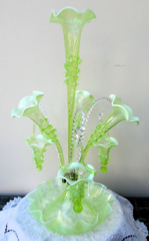 fig 1. A Victorian light green art glass epergne featuring a tall central trumpet vase, surrounding trumpet arms with hanging baskets, and a ruffled bowl base.