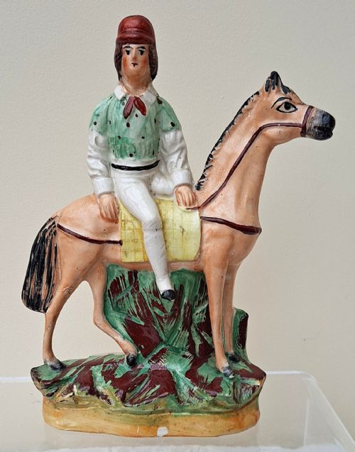 fig 1. A pair of antique Victorian Staffordshire ceramic figures depicting jockeys in green spotted jackets mounted on tan horses.